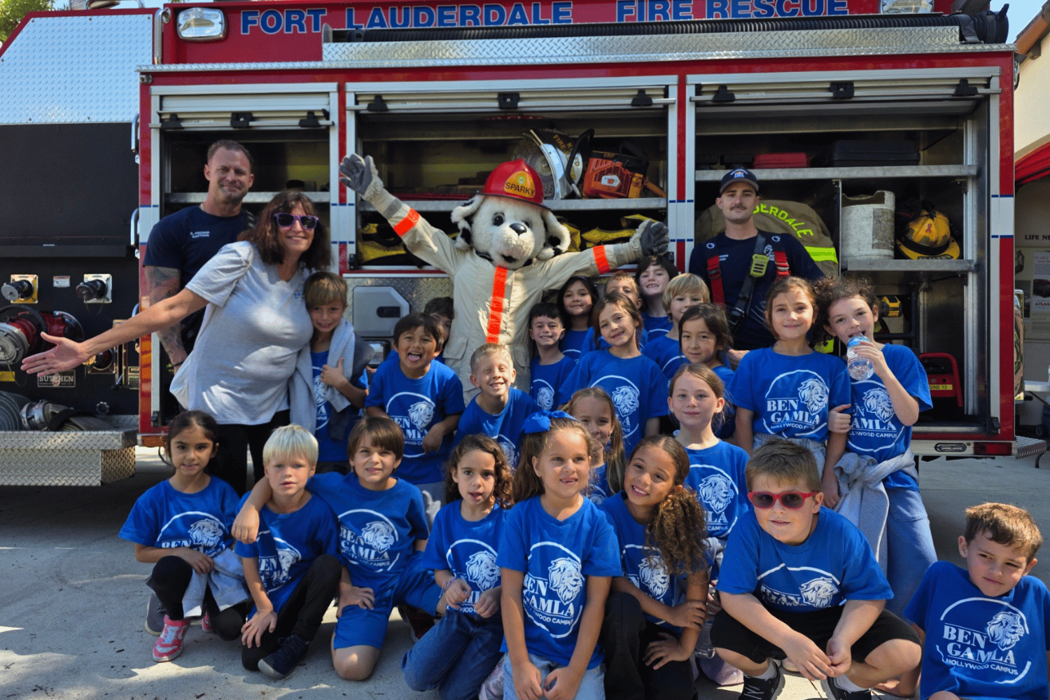 Elementary school students posing with firefighters and Sparky the Fire Dog mascot in front of a Fort Lauderdale Fire Rescue truck during a museum field trip.