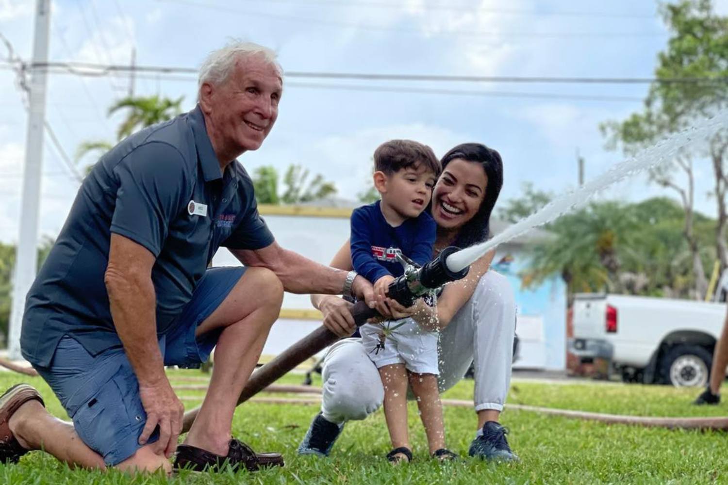 fort-lauderdale-fire-museum-family-fire-safety-activity Child learning fire safety with a volunteer firefighter at the Fort Lauderdale Fire and Safety Museum, assisted by a parent during a hands-on hose activity.